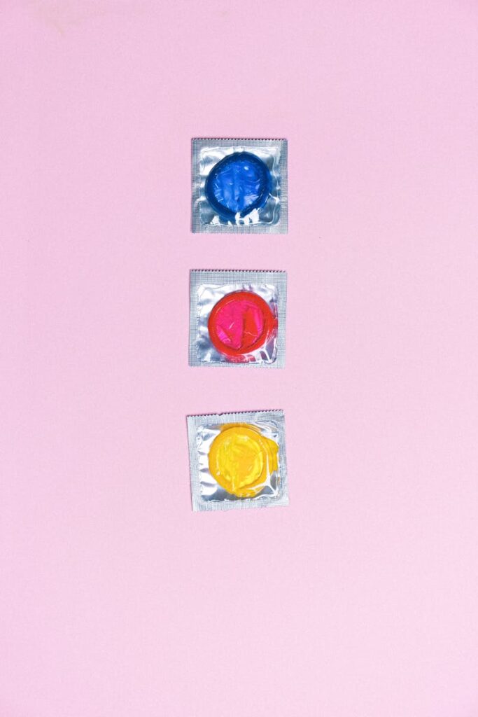 Top view arrangement of multicolored latex condoms composed in row on light pink surface